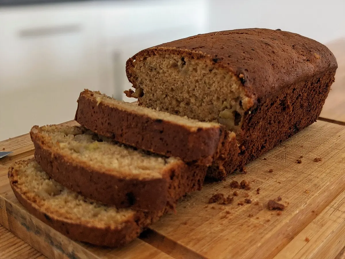 Bolo de banana caseiro em formato de pão, cortado em fatias sobre uma tábua de madeira