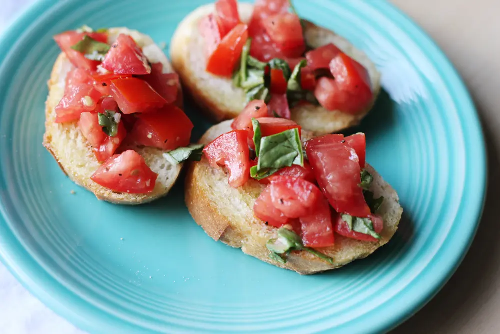 Torradas cobertas com tomate picado e folhas de manjericão num prato azul