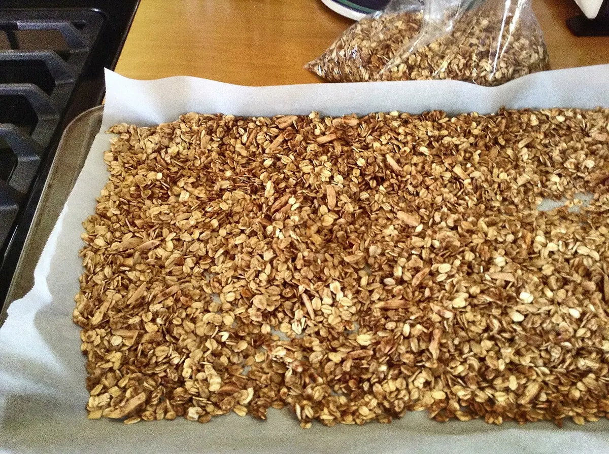 Granola caseira de aveia tostada espalhada numa assadeira forrada com papel-manteiga