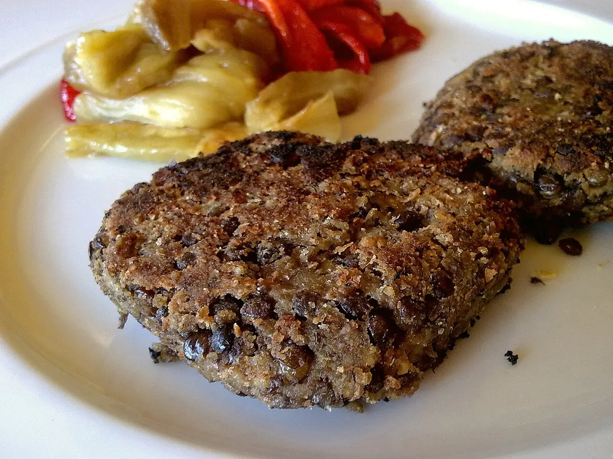 Hambúrgueres caseiros de lentilha dourados num prato com legumes assados
