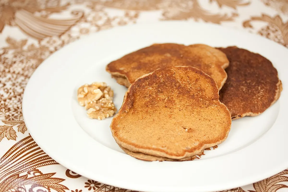 Panquecas douradas de banana empilhadas num prato branco, com nozes ao lado