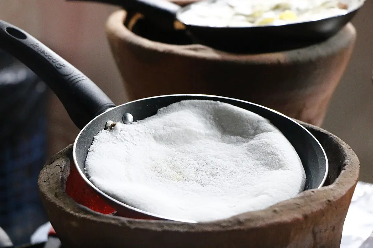 Massa de tapioca branquinha cozinhando numa frigideira pequena sobre fogareiro de barro
