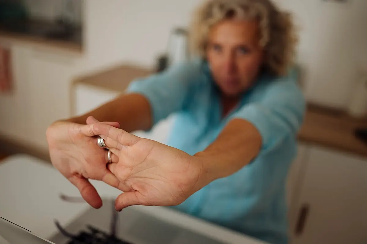 Mulher sentada à mesa de trabalho alongando os braços e os dedos para a frente
