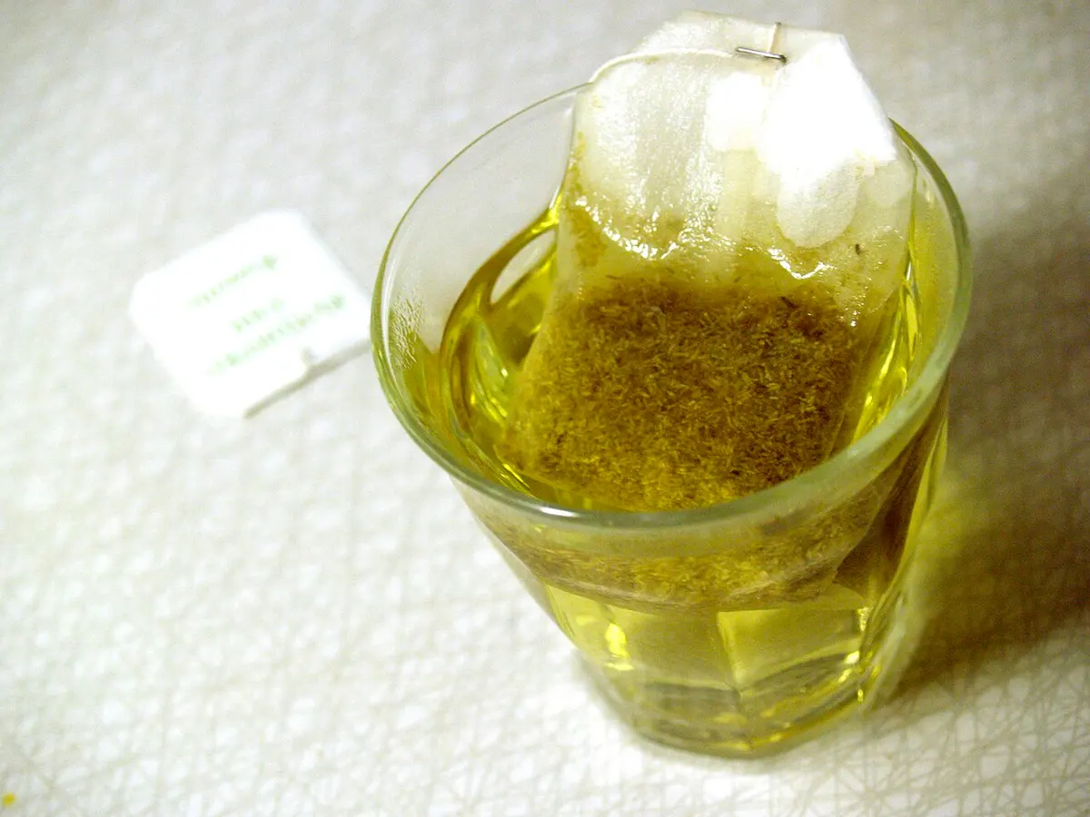 Copo de vidro com chá de camomila dourado e o sachê em infusão