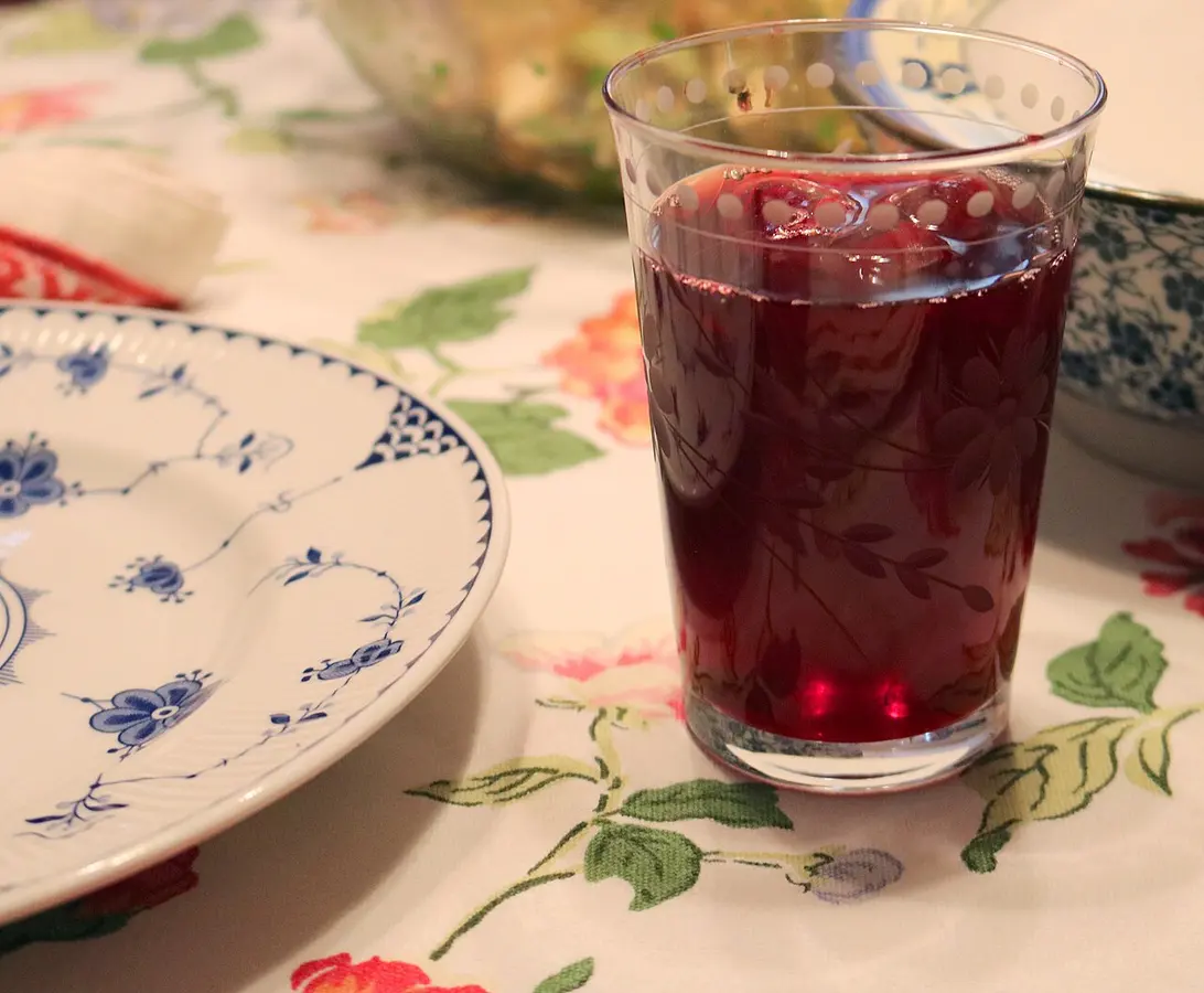 Copo de chá de hibisco vermelho-escuro sobre uma toalha de mesa florida