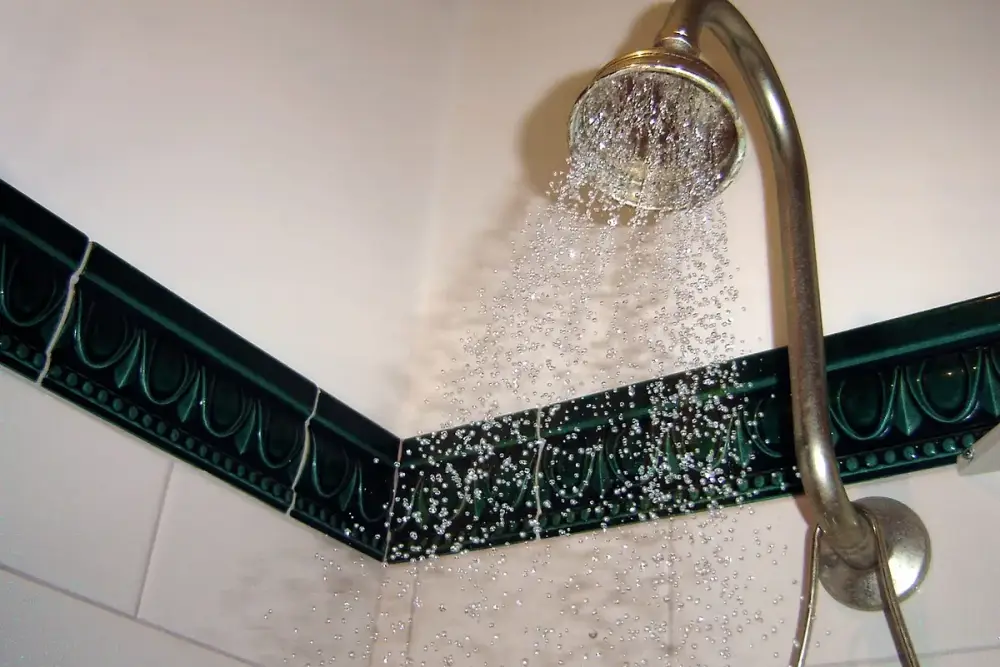 Chuveiro aberto com a água caindo em um banheiro de azulejos claros
